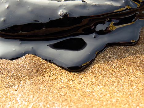 A closeup view of the oil from a ship tanker oil spill in the sea getting into the sand on a beach