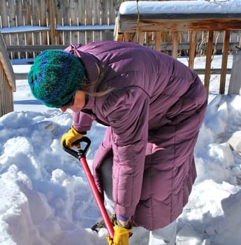 Mature female shoveling winter snow outside.