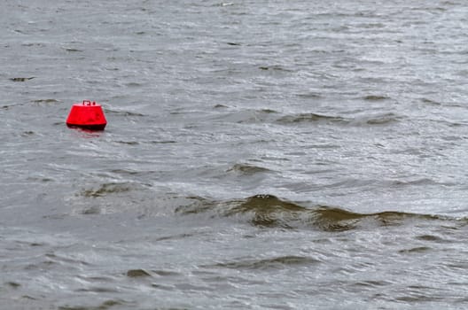 View from a boat on the water in bad weather. In the foreground a red buoy.