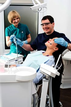 Male dentist treating patient teeth with assistant