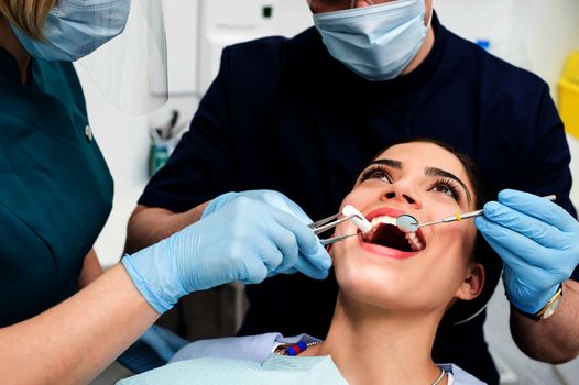 Dentist treating patient teeth with assistant