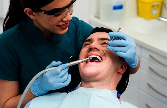 Female dental assistant treat male patient in clinic