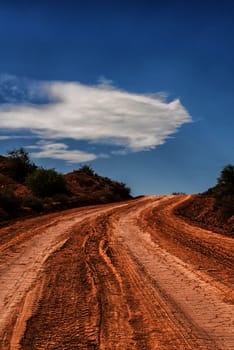 looking up desert dirt road, cloudy blue sky behind