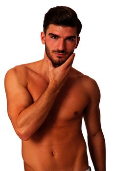 Handsome shirtless naked bearded young man standing looking intently at the camera with his hand to his chin in a sensual sexy pose, isolated on white