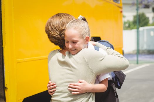 Mother hugging her daughter by school bus outside the elementary school