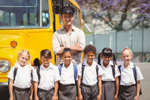 Cute pupils with their school bus driver outside the elementary school