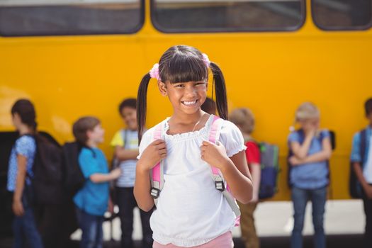 Cute pupils smiling at camera by the school bus outside the elementary school