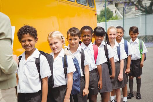 Cute schoolchildren waiting to get on school bus outside the elementary school