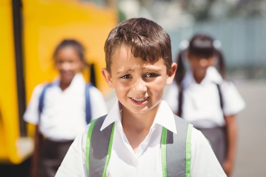 Cute pupil smiling at camera by the school bus outside the elementary school