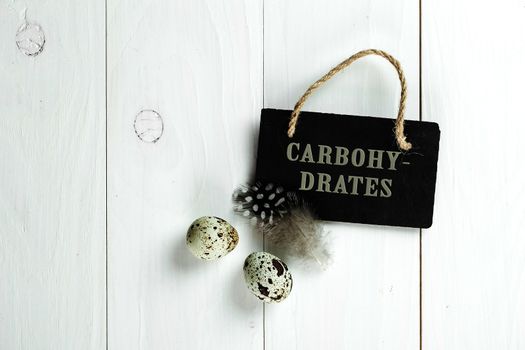Quail eggs and feather with vintage blackboard on white wooden background, with copy space for greeting text.