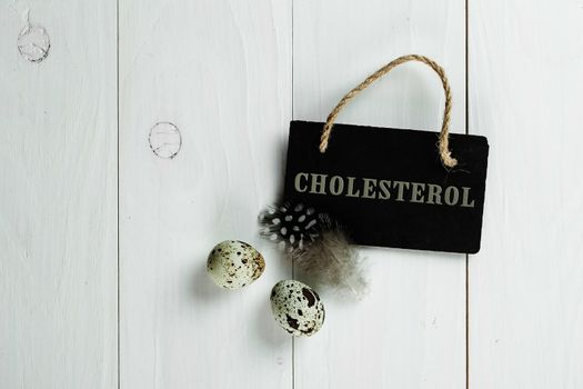 Quail eggs and feather with vintage blackboard on white wooden background, with copy space for greeting text.