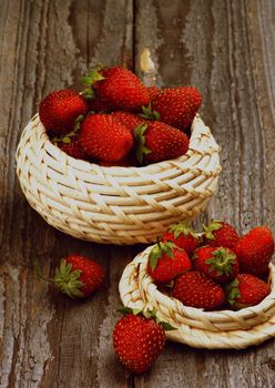 Fresh Forest Strawberries in Wicker Bowls closeup on Rustic Wooden background. Retro Styled