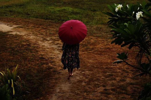 Girl in oriental suit in tropical garden with red umbrella