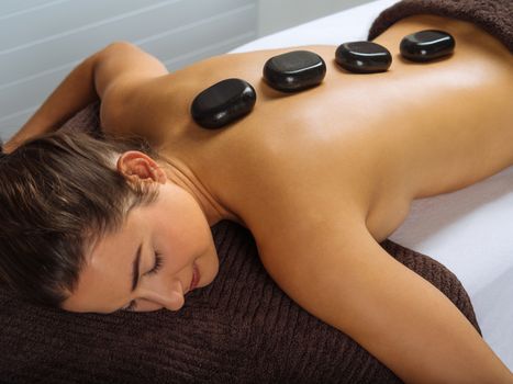 Photo of a young woman lying in a spa having a hot stone treatment. Focus on the first two stones.