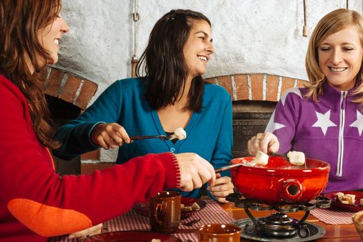 Photo of three beautiful females dipping bread into the melted cheese in a fondue pot.