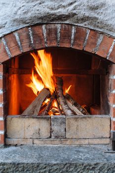 Photo of an outdoor brick fireplace with a fire blazing inside.
