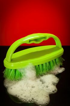 Green brush with coarse bristles with soapsuds photographed in a studio against a red background