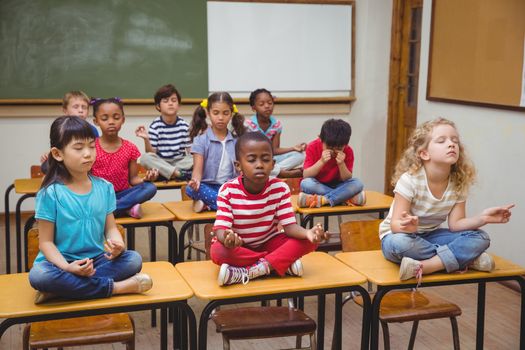 Pupils meditating in lotus position on desk in classroom at the elementary school