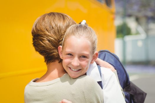 Mother hugging her daughter by school bus outside the elementary school