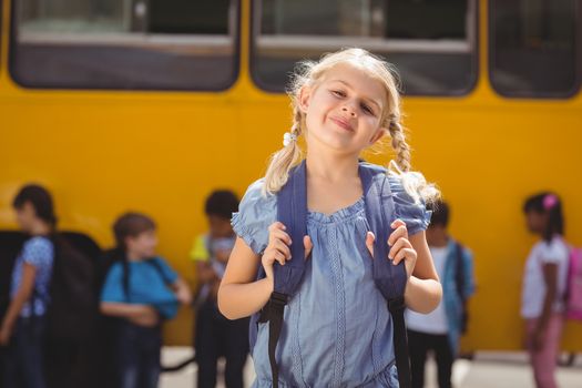 Cute pupils smiling at camera by the school bus outside the elementary school