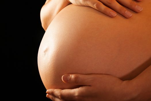 Close-up on the abdomen of a pregnant naked woman holding it on black background, isolated with work path.