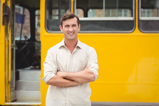 Smiling bus driver standing with arms crossed in front of his bus