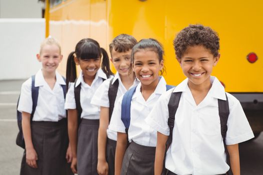 Cute schoolchildren smiling at camera by the school bus outside the elementary school