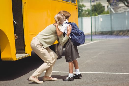 Mother hugging her daughter by school bus outside the elementary school