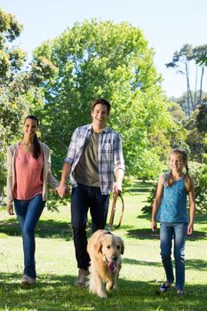 Happy family walking their dog in the park on a sunny day