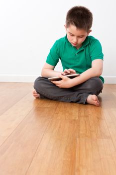 Cute 10 Year Old Male Kid Sitting on the Floor with Legs Crossed, Playing at his Portable Tablet Computer Seriously.