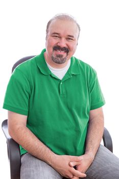 Portrait of a Smiling Bearded Middle Age Man, Wearing Plain Green Polo Shirt, Sitting on a Chair with Hands Crossed. Isolated on White Background.