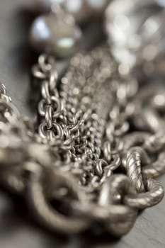 Assorted silver costume jewellery with a jumbled pile of chains with different shaped links, a clear crystal bead and a necklace of round silver beads with focus to the chains