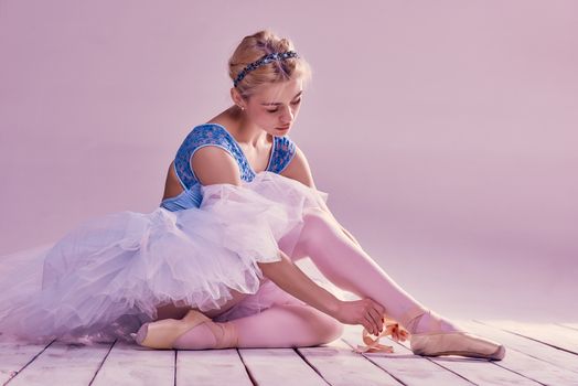 Professional ballerina putting on her ballet shoes on the wooden floor on a pink background