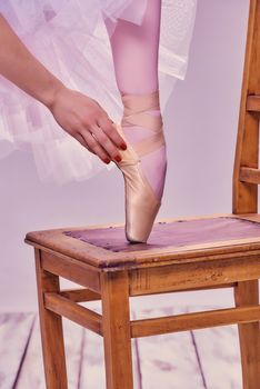 Professional ballerina putting on her ballet shoes.on the  wooden chair on a pink background. feet close-up