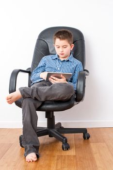 Busy Young Handsome Boy with Tablet Computer Sitting on a Black Office Chair with Legs Crossed and Bare Feet.