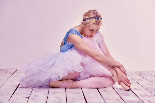 Tired ballet dancer sitting on the wooden floor on a pink background