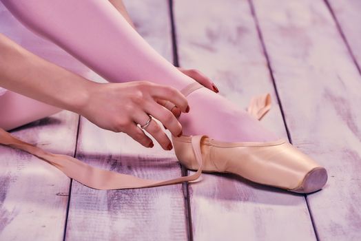 Professional ballerina putting on her ballet shoes on the wooden floor on a pink background. feet close-up