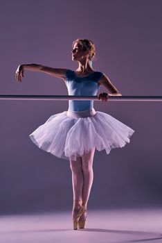 classic ballet dancer in white tutu at ballet barre on a lilac background