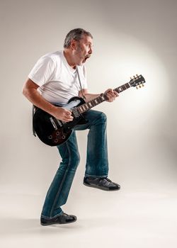 Full length portrait of a guitar player exciting music on gray background