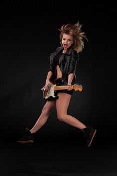 Beautiful jumping blonde girl playing guitar in rock style on a black background