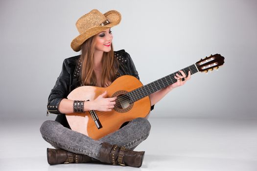 The beautiful girl in a cowboy's hat playing acoustic guitar on a gray background