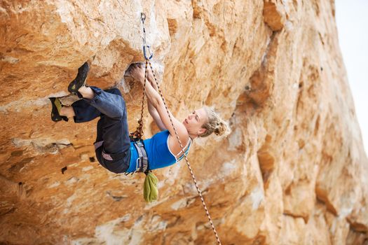 Young female rock climber struggling to make next movement up