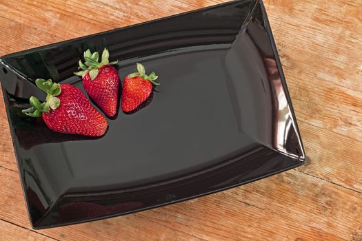 three red strawberries in a black plate and wooden base