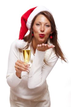 Playful woman wearing a festive red Santa hat and holding a flute of champagne celebrating Christmas blowing a kiss across the palm of her hand with a mischievous smile, on white