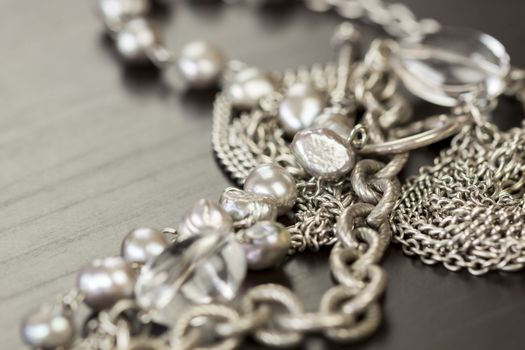 Assorted silver costume jewellery with a jumbled pile of chains with different shaped links, a clear crystal bead and a necklace of round silver beads with focus to the chains