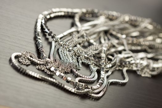 Pile of assorted silver chains with shiny box chains, cube chains and ordinary linked chain on a grey background conceptual of fashion jewellery