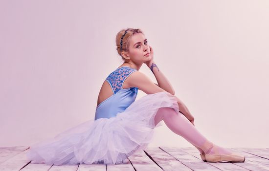 Tired ballet dancer sitting on the wooden floor on a pink background