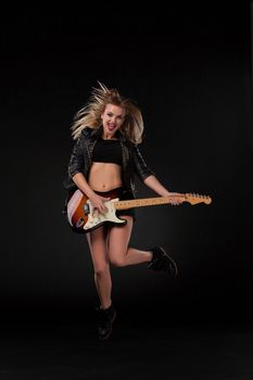 Beautiful jumping blonde girl playing guitar in rock style on a black background