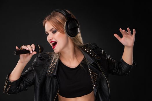 Portrait of a beautiful blonde young woman singing into microphone with headphones in studio on black background