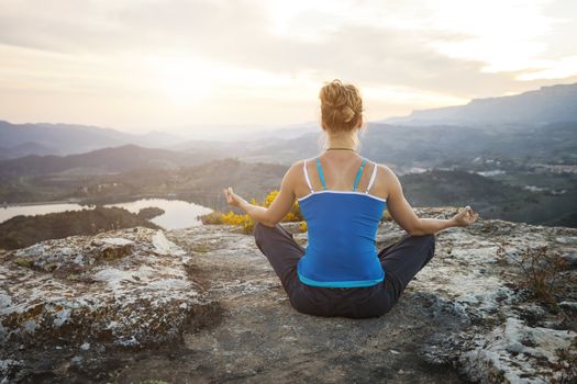 Young woman sitting on a rock and enjoying valley view. Girl sits in asana position.